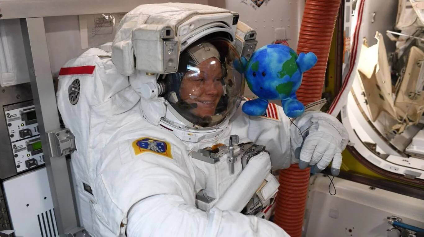 Astronauta con un tierno peluche de la Tierra en el espacio